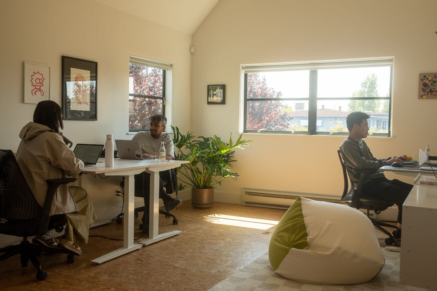 Três pessoas trabalhando em computadores, em um cômodo iluminado pelo Sol.